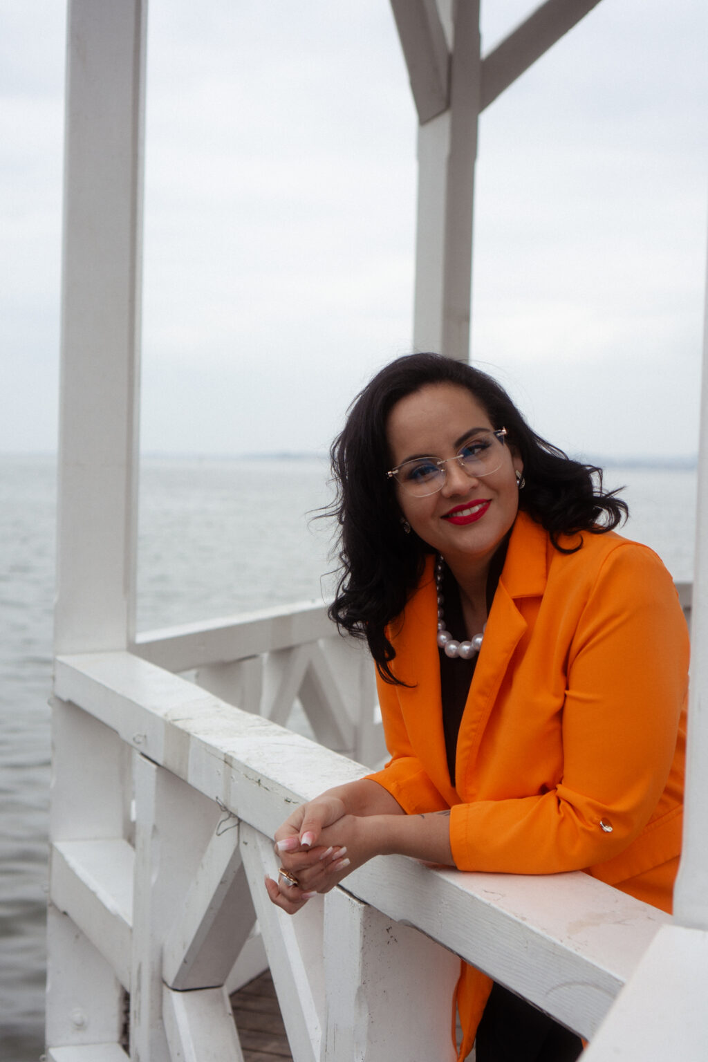 Juliem Rechmann im orangen Blazer mit Perlenkette am See